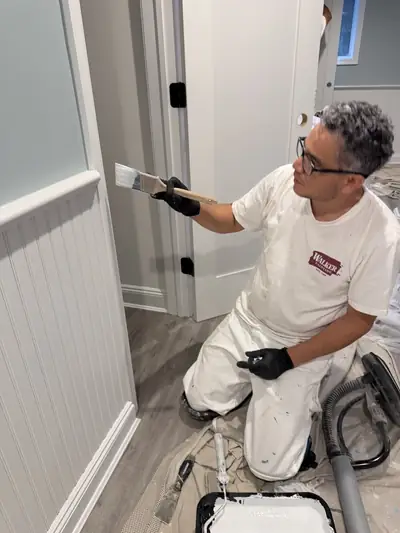 Painter kneeling to brush the last inch of baseboard trim